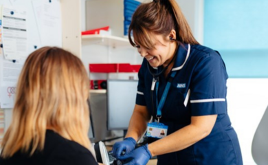 A nurse stands and engages in conversation with a patient in a hospital setting.