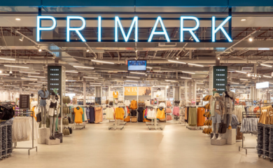 Image of the entrance to a Primark store with the brand name at the top and rails of clothes inside
