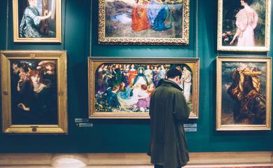 A man stands in an Art Gallery Looking at Paintings