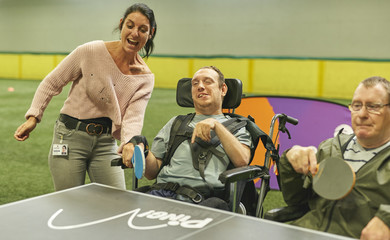 Two men in wheelchairs and a lazy standing up, playing table tennis