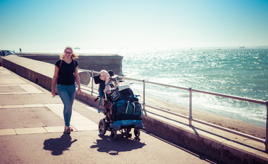 Man in a wheelchair with lady walking beside him along a seafront