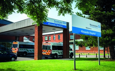 Image shows the exterior of Alexandra Hospital. There are two ambulances and a black car outside the entrance. There is a sign that says Worcestershire Acute Hospitals NHS Trust and Welcome to Alexandra Hospital. 