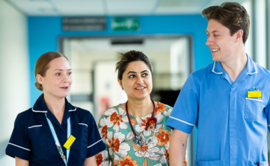 Image of 3 people: 2 women and a man walking down a hospital corridor smiling and talking to each other.