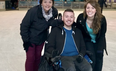 Image of Ross sitting in his wheelchair ice skating with two people next to him.